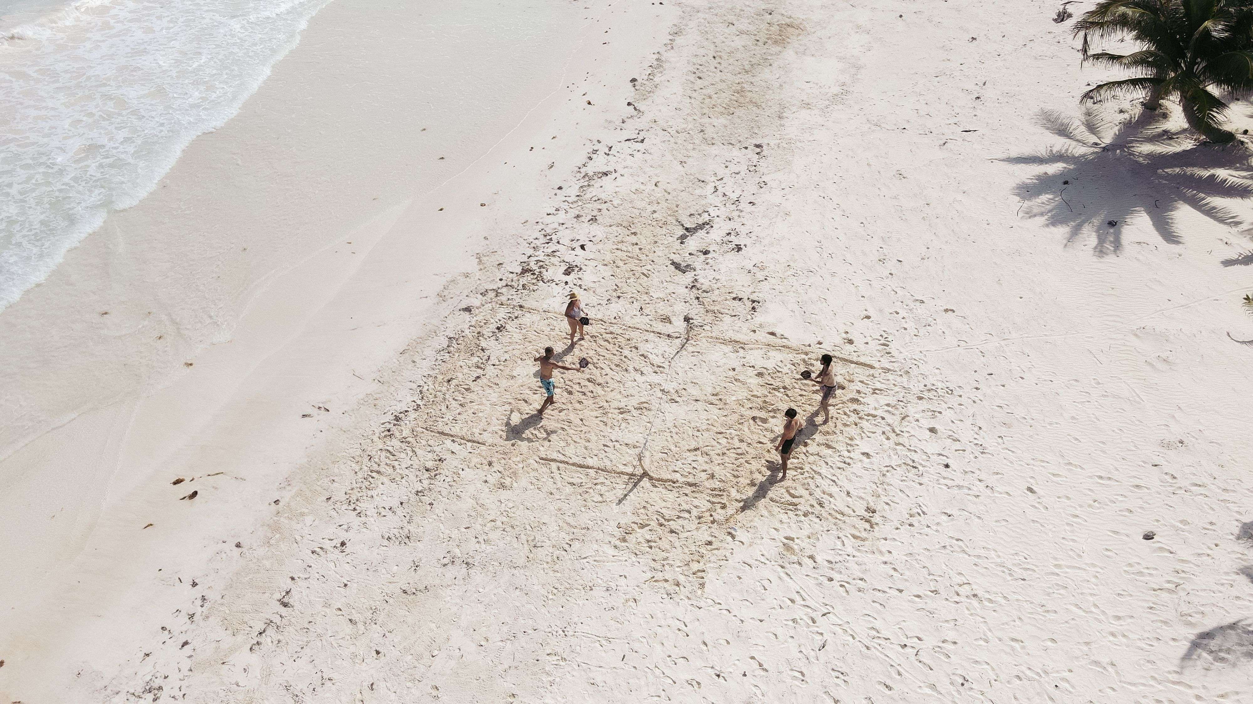 Aerial view of four people playing volleyball on a white sand beach by the ocean