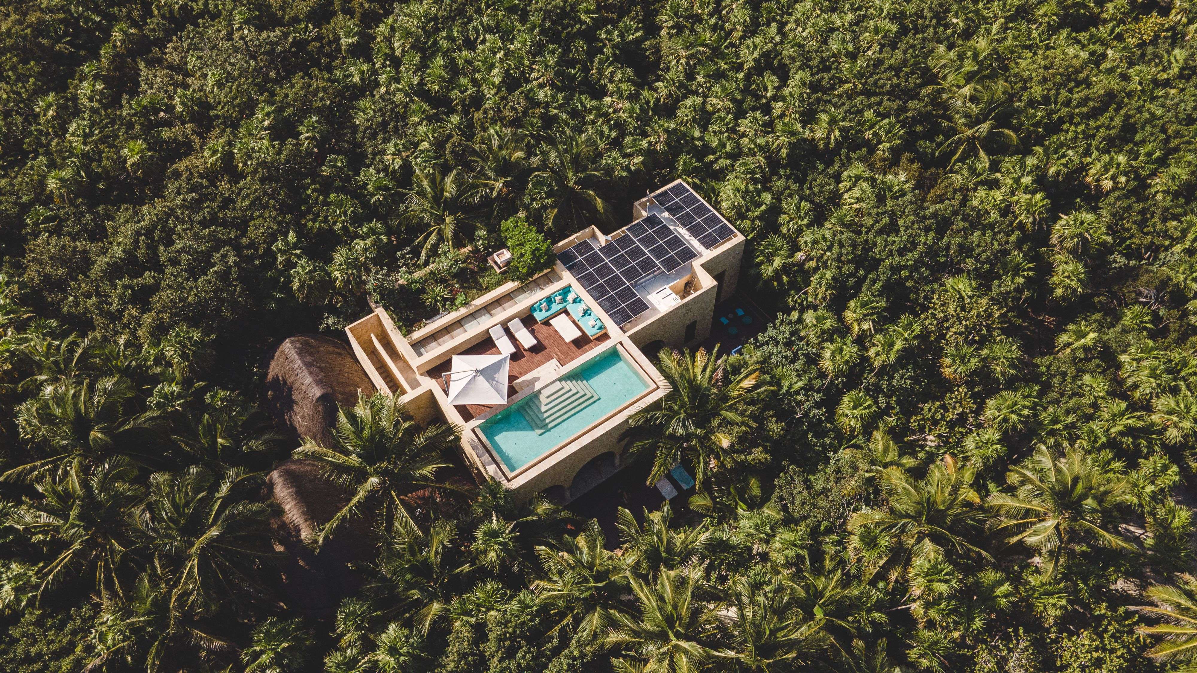 Aerial view of a secluded villa with a pool and solar panels in a lush tropical forest